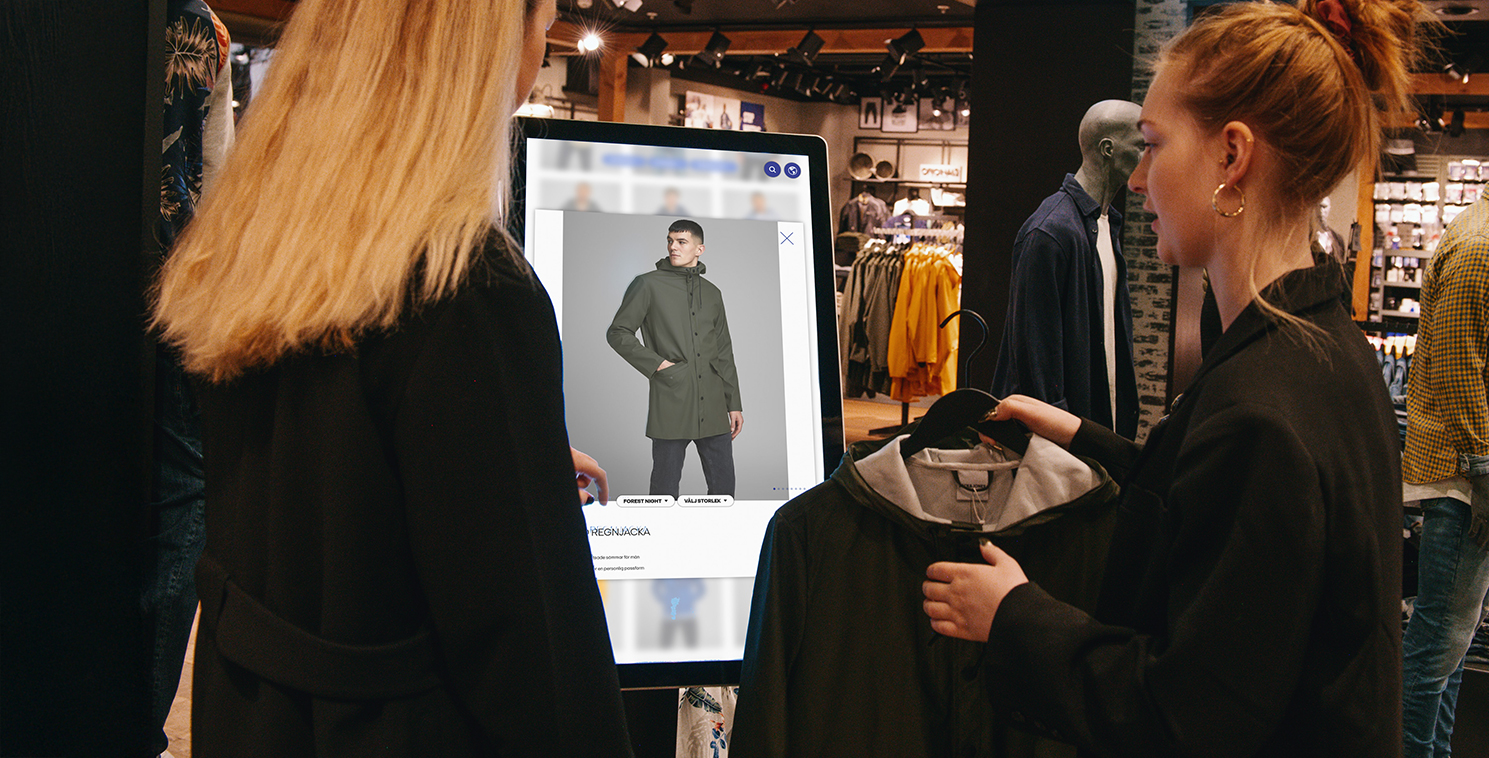 Two shoppers use a large touchscreen display in a retail store to explore virtual clothing options, showcasing experiential retail technology and personalized in-store engagement.