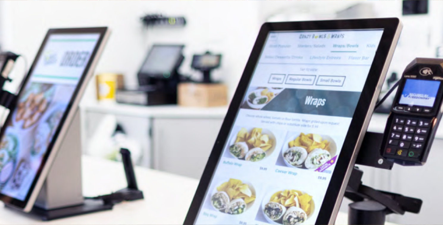 Close-up of Elo touchscreen kiosks in a quick-service restaurant displaying digital menus with an integrated payment terminal, showcasing streamlined self-service ordering and checkout.